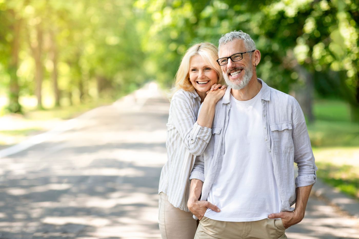 Older couple smiling together on a tree-lined path